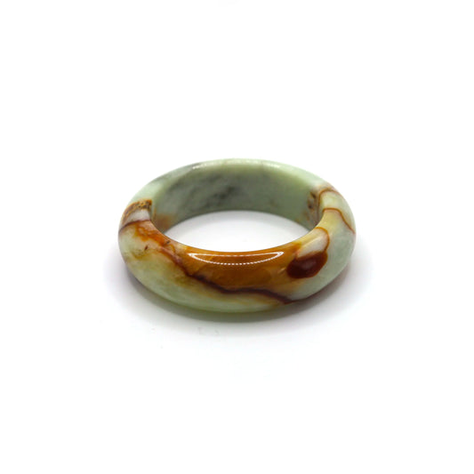 Pale green jade bangle with vivid red vein inclusions resting on neutral fabric Miruzi