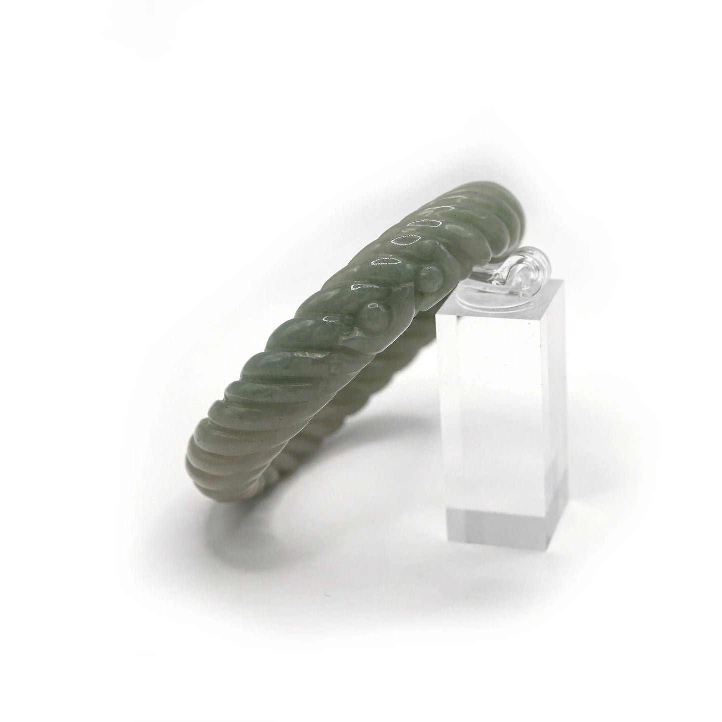 A tactile jade bracelet designed in a smooth, spiraling curve, highlighted by delicately carved symbols of abundance – Miruzi