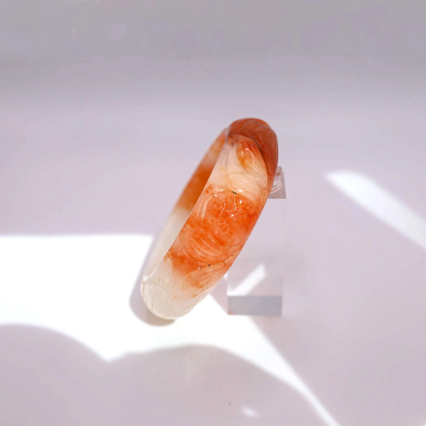 Orange and white jade bangle with symbolic lotus and goldfish carving, symbolizing purity and abundance