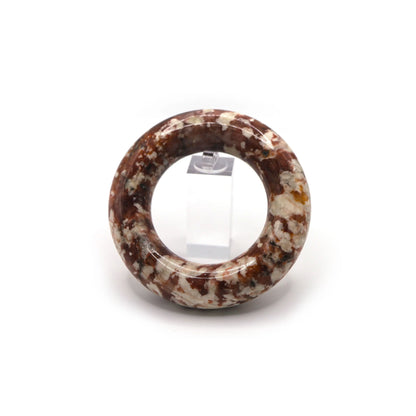 Donut-style red jade bracelet resting on neutral silk, with clustered white inclusions giving a playful yet elegant finish – Miruzi