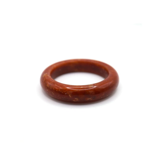 Deep red jade bangle with golden and ivory veining placed on neutral fabric
