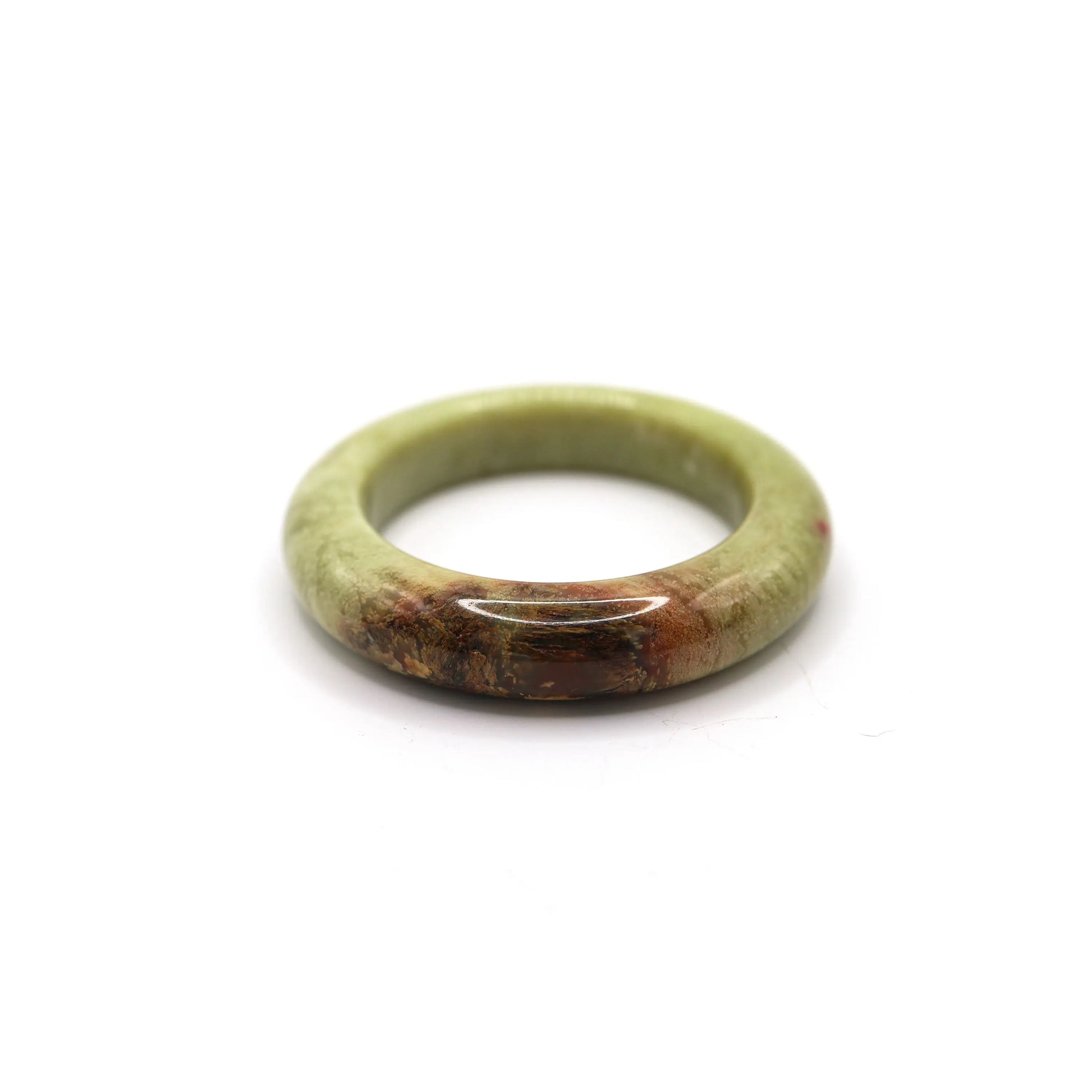 Green yellow jade bangle with warm tones and red-brown veining placed on neutral fabric Miruzi