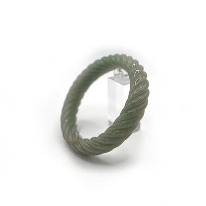 Hand-carved twisted jade bangle with fluid spiral form and ancient coin carvings, offering motion, luck, and elegant tradition – Miruzi
