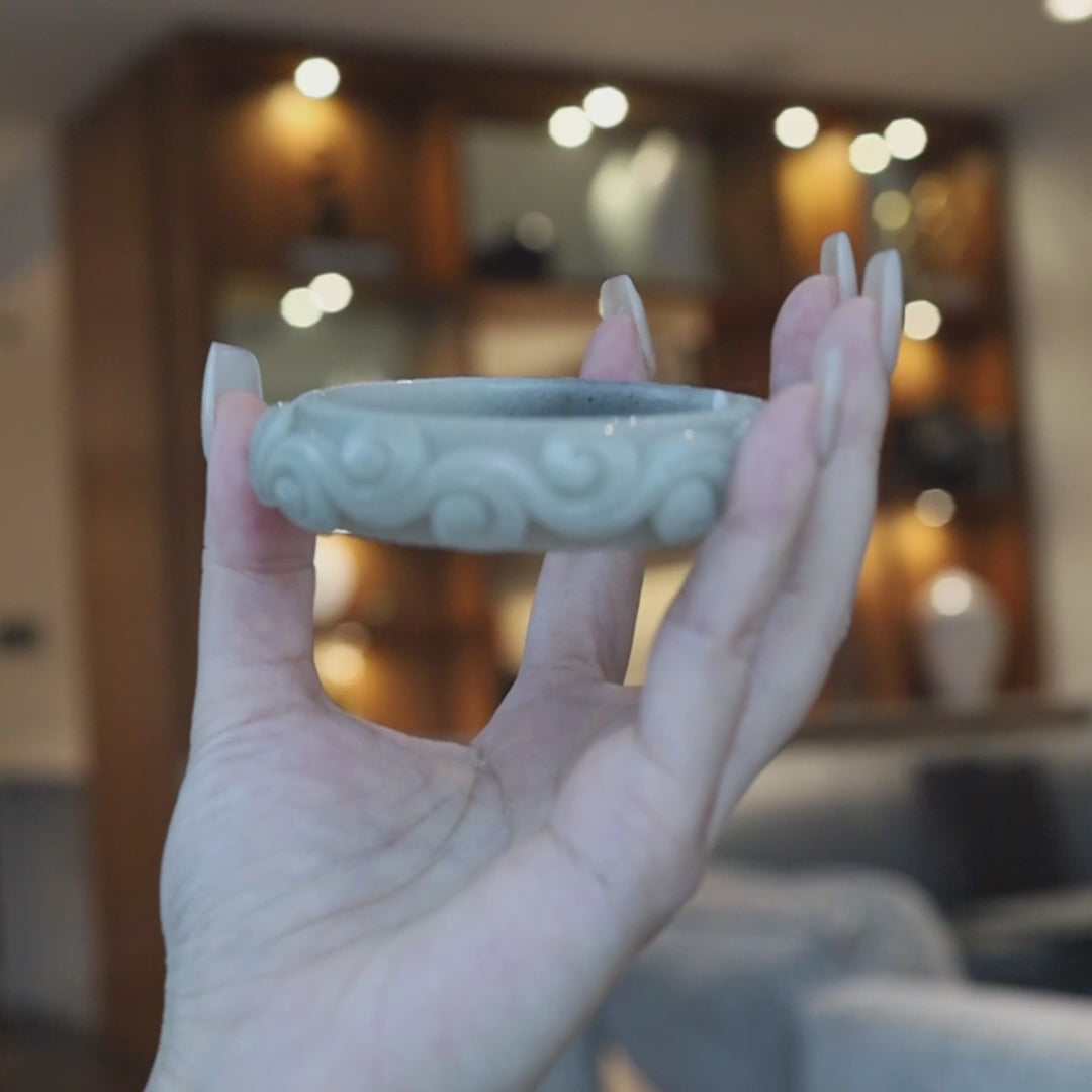 Hand-carved jade bracelet in soft green quartzite with a smoky black peony blossom, surrounded by raised cloud patterns and engraved circular detailing for a serene, symbolic finish – Miruzi