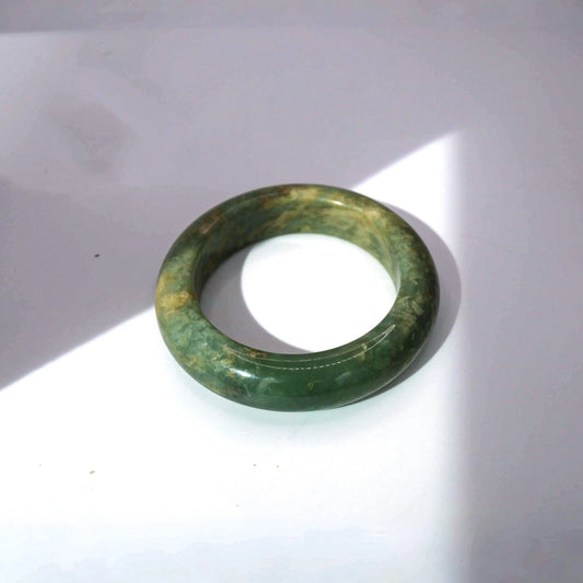Yellow green jade bangle with natural marbled patterns in muted ochre and soft green tones, full round form


